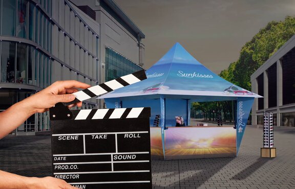 A woman is holding a flap in front of the promotion tent. The promotion tent is standing in the dark and is illuminated.