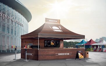 Gazebo pieghevole marrone con stampa su tutta la superficie come stand di vendita per hamburger davanti ad una fiera.