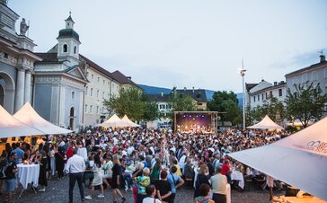 Faltpavillons mit Vordach beim Dine, Wine and Music auf dem Domplatz in Brixen. Die Gäste genießen den Abend. Im Hintergrund sieht man die Band auf der Bühne.