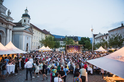Diversi gazebo per eventi nella piazza del Duomo di Bressanone al Dine & Wine festival. La gente è seduta e festeggia.