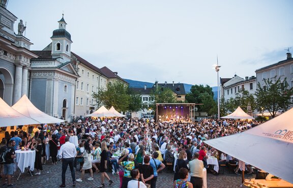 Faltpavillons mit Vordach beim Dine, Wine and Music auf dem Domplatz in Brixen. Die Gäste genießen den Abend. Im Hintergrund sieht man die Band auf der Bühne.