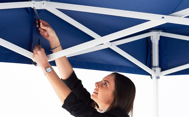 Frau klipst das Dach des blauen Faltpavillons an, damit es optimal gespannt ist.