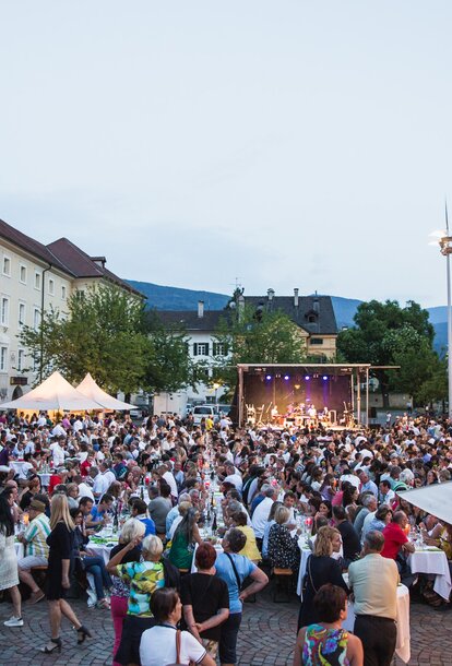 Kilka białych namiotów eventowych o wymiarach 3x3 m z zadaszeniami na placu katedralnym w Brixen podczas festiwalu Dine & Wine. Ludzie siedzą i świętują. Namioty dla stowarzyszeń i gmin.