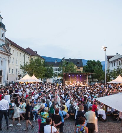 Diversi gazebo per eventi bianchi 3x3 m con tettoie nella piazza del Duomo di Bressanone al Dine & Wine festival. La gente è seduta e festeggia. Gazebo per associazioni e comuni.