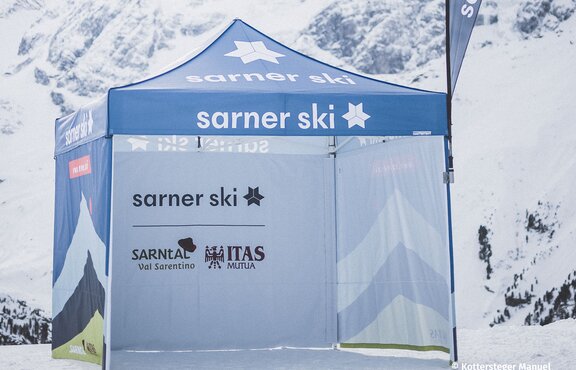 The fully printed Sarner Ski promotion tent in the middle of the snowy mountains. It has printed side walls and a promotional flag. | © Kottersteger Manuel