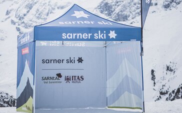 Il gazebo promozionale di Sarner Ski, completamente stampato, in mezzo alle montagne innevate. Ha le pareti laterali stampate e una bandiera pubblicitaria. | © Kottersteger Manuel