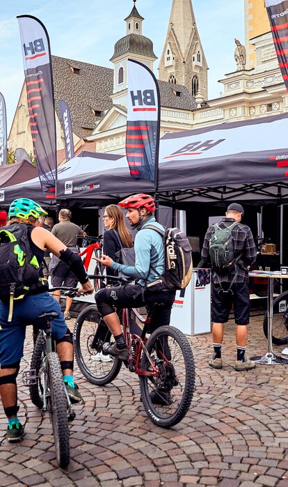 Promotionzelte von BH bei einem Bike-Festival auf dem Domplatz in Brixen. Das Zelt hat viele Fahnen. Davor befinden sich Mountainbiker.