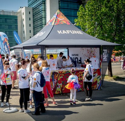 Vollfächig bedrucktes Promotionzelt von Kafune bei einem Event. Der Faltpavillon hat Eckfahnen. Besucher stehen in weißen Tshirts vor dem Promotionzelt.