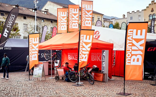 Gazebo pieghevole promozionale arancione 4,5x3 m  Mountainbike con bandiere e parete laterale arancione personalizzata con logo. 
