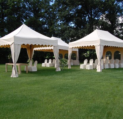 Three white gazebos are standing in the meadow. Underneath the gazebos are chairs with overcoat. 