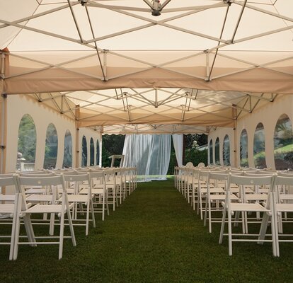 Il gazebo pieghevole a forma di pagoda viene utilizzato ad un matrimonio. Sotto il gazebo pieghevole ben decorato ci sono delle sedie.