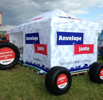 Gazebo pieghevole bianco personalizzato ad una fiera agricola. Di fronte al gazebo si trovano delle ruote di un trattore.