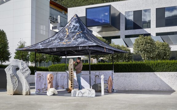 Il gazebo pieghevole con tettoia è completamente personalizzato. È posizionato di fronte ad un edificio moderno e sotto il gazebo pieghevole c' è uno scalpellino.