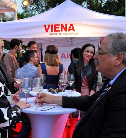 White party 3x3m tent with the label "Viena" is in the background. In front of it are guests drinking Prosecco.