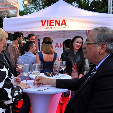 Weißes Partyzelt mit der Aufschrift "Viena" steht im Hintergrund. Davor befinden sich die Gäste und trinken Prosecco.
