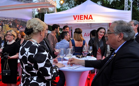 Partyzelte für jedes Event Weißes Partyzelt mit der Aufschrift "Viena" steht im Hintergrund. Davor befinden sich die Gäste und trinken Prosecco.