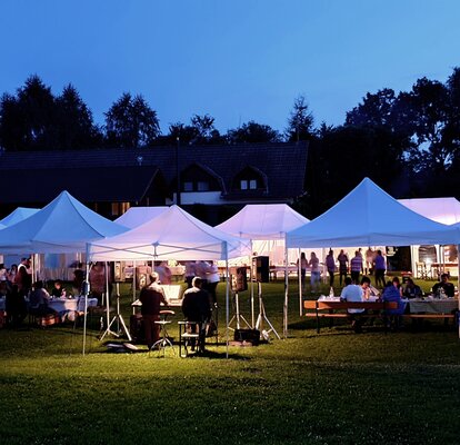 Partyzelte im Garten Weiße Partyzelte in verschiedenen Größen im Garten. Darunter sitzen Menschen und feiern.