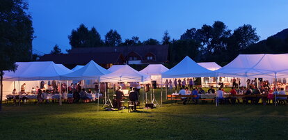 Serata con diversi gazebo bianchi e tavoli e sedie da giardino immersi nel verde.