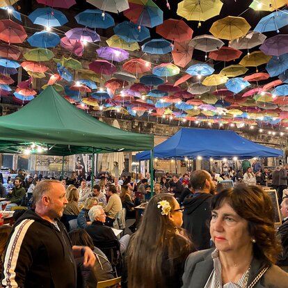 Mercato animato con ombrelli colorati come decorazione del soffitto e due gazebo pieghevoli in verde e blu.