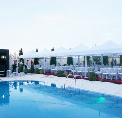 Faltpavillons für Cateringevents Die weißen Faltpavillons sind dank des Baukastensystems miteinander verbunden. Sie stehen alle am Pool. Darunter befinden sich runde Tische für ein Dinner.
