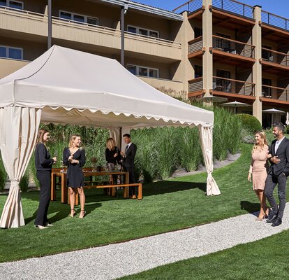 Un gazebo pieghevole elegante die MASTERTENT si trova di fronte ad un albergo. Gli ospiti sono vestiti in modo elegante e si trovano vicino al gazebo.