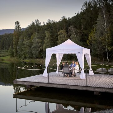Weißer Faltpavillon steht auf dem Steg am See. Darunter dinieren 4 Personen.