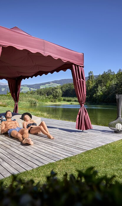 Il kit Royal color bordeaux di fronte al lago. Una coppia prende il sole sotto il gazebo.