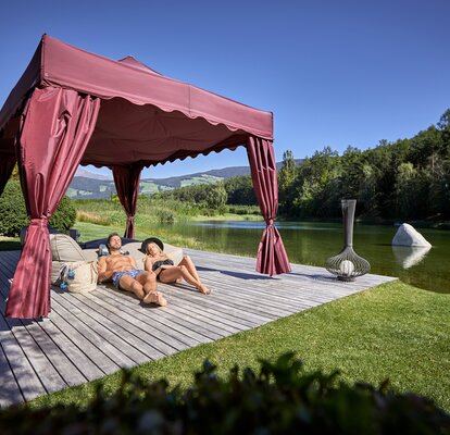 Il kit Royal color bordeaux di fronte al lago. Una coppia prende il sole sotto il gazebo.