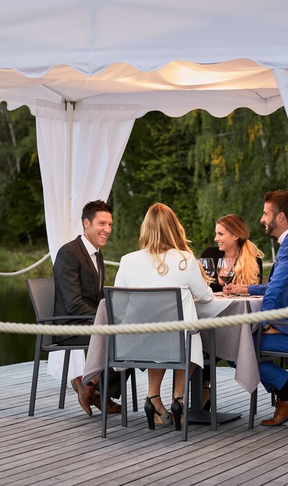 Die 4 Gäste sitzen unter dem Faltpavillon beim Abendessen.