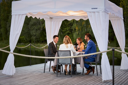 Die 4 Gäste sitzen unter dem Faltpavillon beim Abendessen.