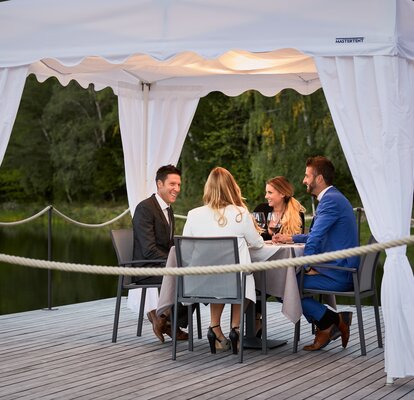 Die 4 Gäste sitzen unter dem Faltpavillon beim Abendessen.