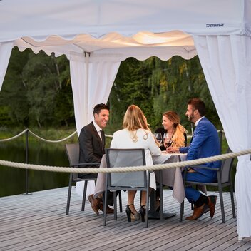 4 guests are sitting under the gazebo. They are having dinner. 