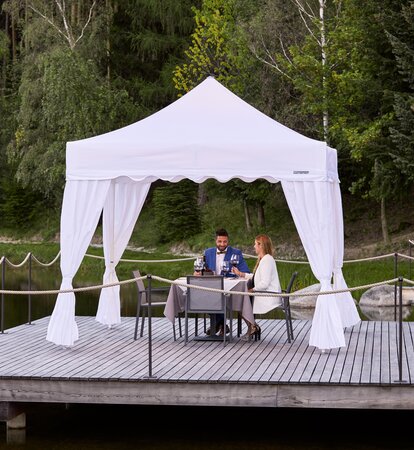 One couple is sitting under the gazebo. The second couple is approaching. Everything is prepared for dinner. 