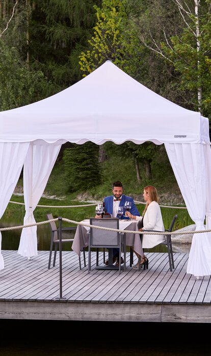 One couple is sitting under the gazebo. The second couple is approaching. Everything is prepared for dinner. 