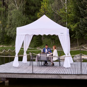 One couple is sitting under the gazebo. The second couple is approaching. Everything is prepared for dinner. 