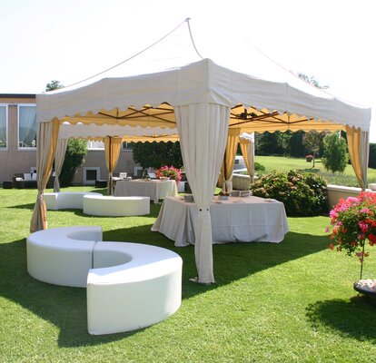 Eleganter Faltpavillon im Garten Eleganter Faltpavillon mit Eckvorhängen bei einer Gartenparty im Freien. Darunter befindet sich eine Sitzgarnitur.