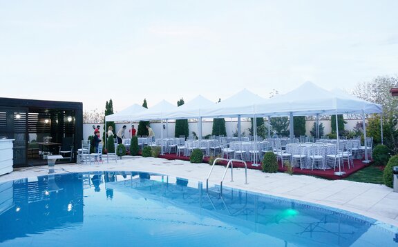 Faltpavillons für Cateringevents Die weißen Faltpavillons sind dank des Baukastensystems miteinander verbunden. Sie stehen alle am Pool. Darunter befinden sich runde Tische für ein Dinner.
