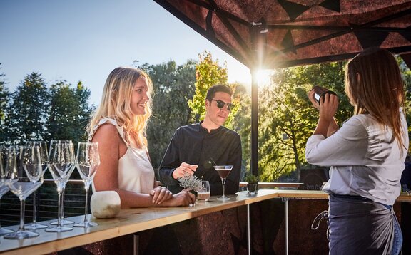 Bancone per gazebo pieghevole La donna sta preparando una bibita dietro il banco per gli ospiti. Gli ospiti si trovano di fronte al gazebo pieghevole durante il tramonto.