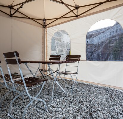 Il gazebo pieghevole visto dall´interno. Ci sono un tavolo e due sedie all´interno della tenda. Si vede la parete laterale con finestra.