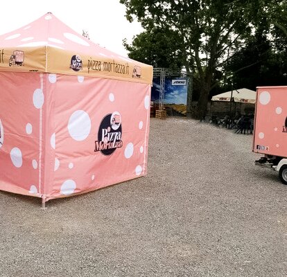 Il gazebo pieghevole per street food "Pizza e Mortazza" è porsonalizzato con il look di una mortadella. Di fianco c' è il furgone con lo stesso look.