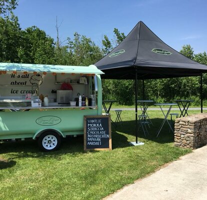 Street Food Stand Der Street Food Stand von "Dingenen & Dergent" steht auf einer Wiese. Der türkisfarbene Anhänger steht neben dem schwarzen Faltpavillon.
