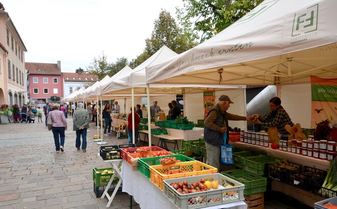 Market tents for a farmers market. In front of them are boxes with fruit and vegetables. 