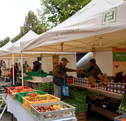 Market tents for a farmers market. In front of them are boxes with fruit and vegetables. 