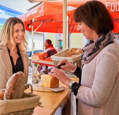 Printed market tent from a baker. Two women are speaking about the products.