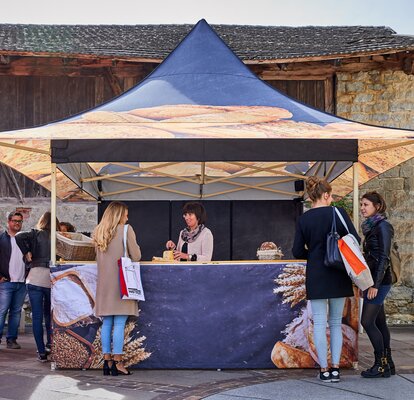 Esta carpa plegable para mercados es de una panadería y está imprimida en toda la superficie con impresión por sublimación fotorealística. Además, la carpa tiene voladizos y un mostrador.