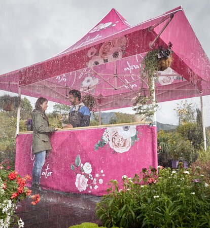 Printed gazebo with awning in the rain. Under the gazebo the customer is buying a flower from the florist. Outside it is raining. 