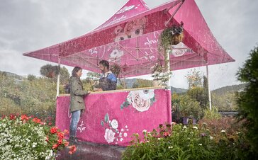 Printed gazebo with awning in the rain. Under the gazebo the customer is buying a flower from the florist. Outside it is raining. 