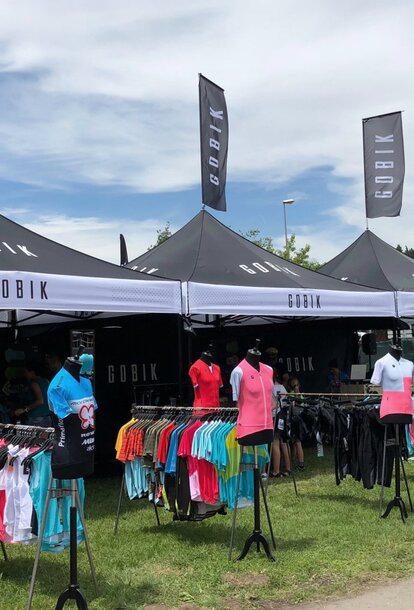 Folding gazebo black 3x3 m customised with logo print, lettering and flags. Black gazebo side walls with white logos and lettering.  Gazebo used as a retail outlet at an event. Retail of T-shirts and sports accessories. 