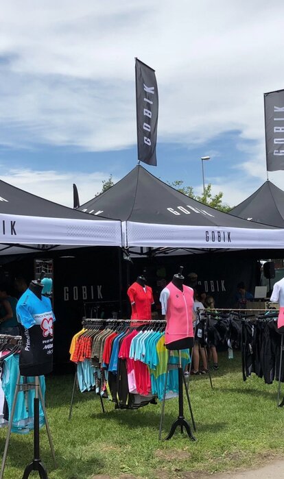 Folding gazebo black 3x3 m customised with logo print, lettering and flags. Black gazebo side walls with white logos and lettering.  Gazebo used as a retail outlet at an event. Retail of T-shirts and sports accessories. 