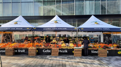 Tres casetas plegables conectadas entre sí con vendedores de fruta y una amplia selección de fruta fresca.